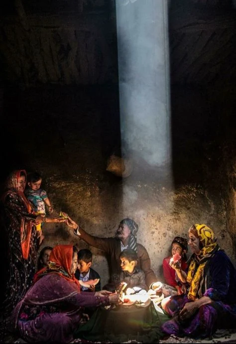 A Kurdish family sharing a meal in a traditional home, illuminated by a shaft of sunlight